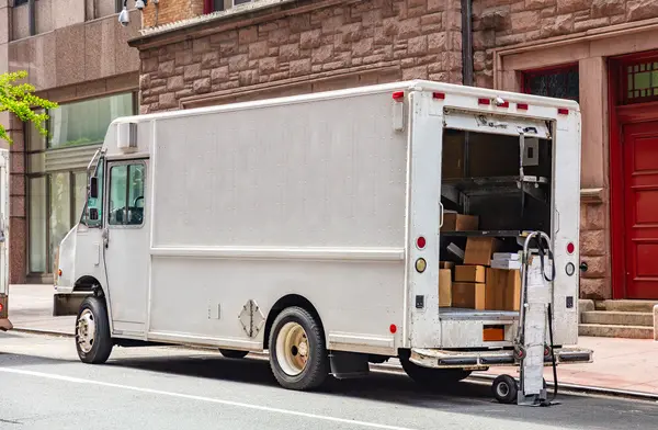 Door to door delivery. Packages in a white color truck with open door, parked on a street downtown, New York