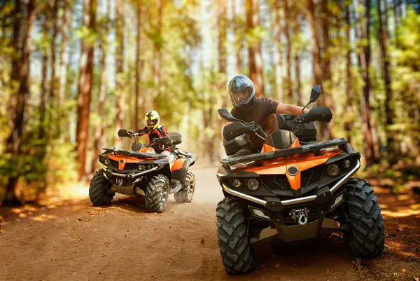 Two atv riders in helmets, speed race in forest, front view. Riding on quad bike, extreme sport and travelling, quadbike offroad adventure